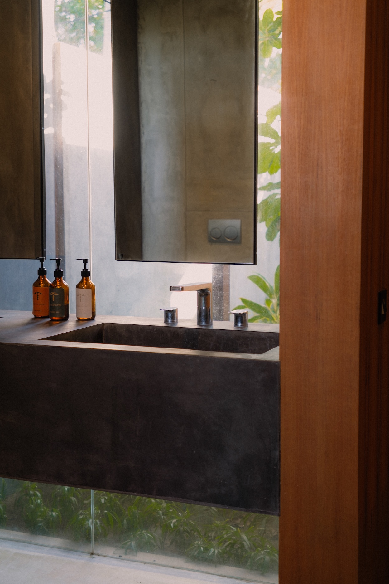 View of cement finished wash basins with glass panels behind looking into gardens