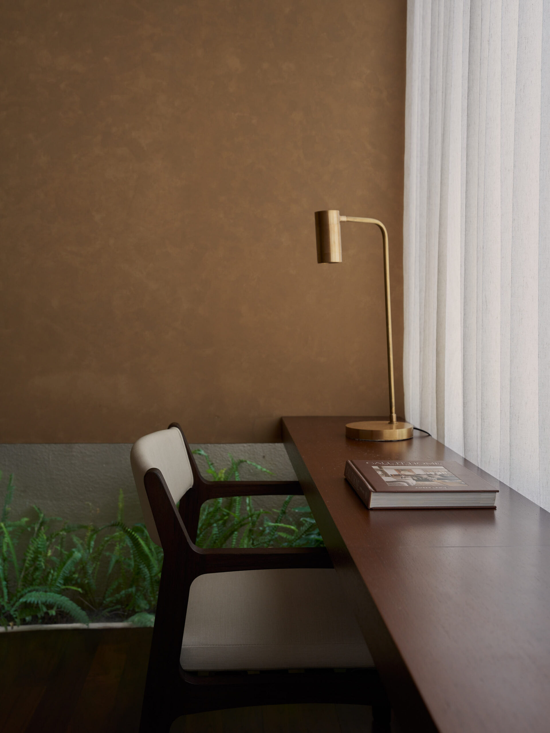 Desk at master bedroom with brushed gold reading lamp and low chair against the window