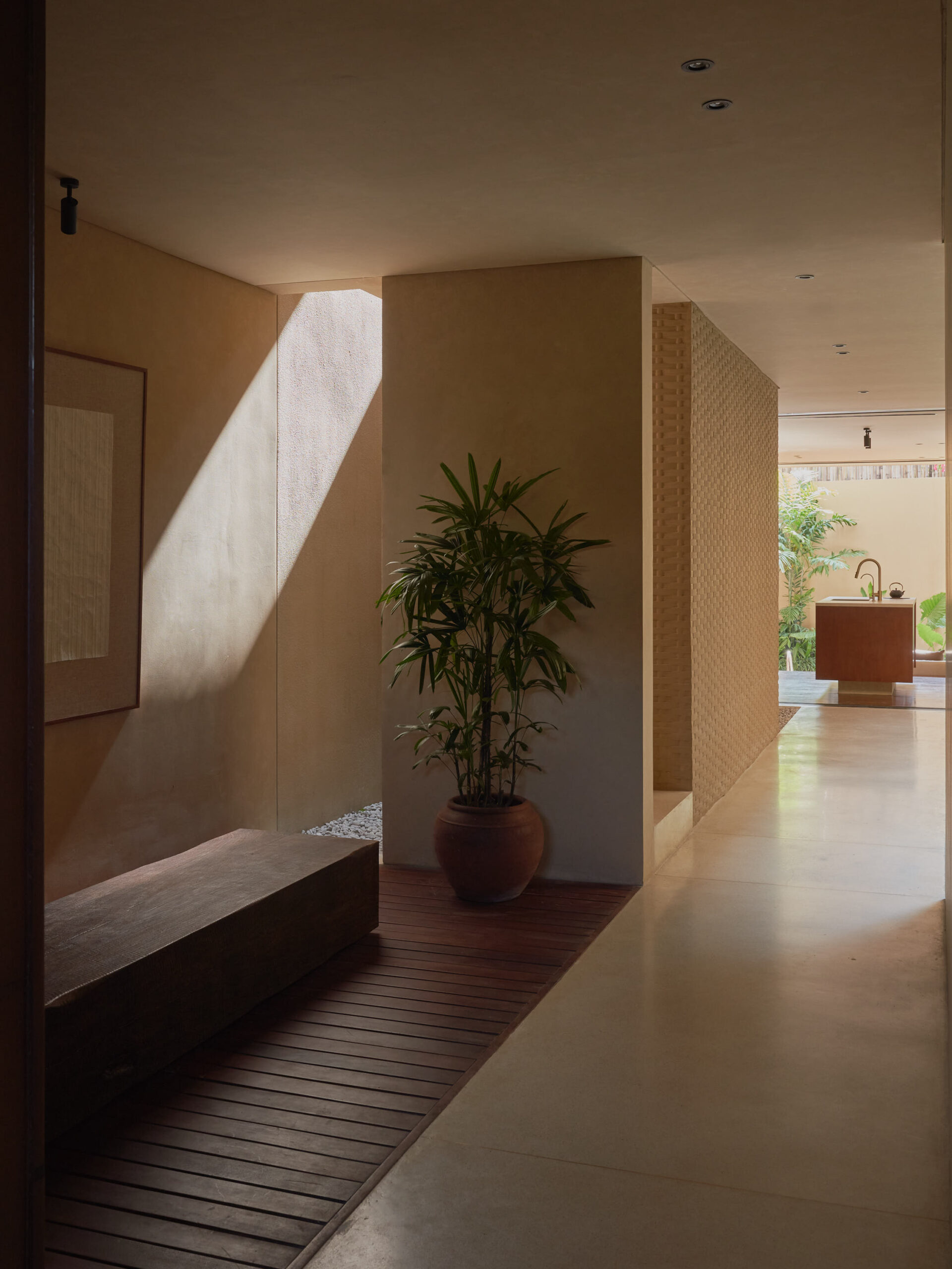 Entrance corridor and foyer at leaf berawa showing solid teak wood bench, banana paper framed art work, and the kitchen island.