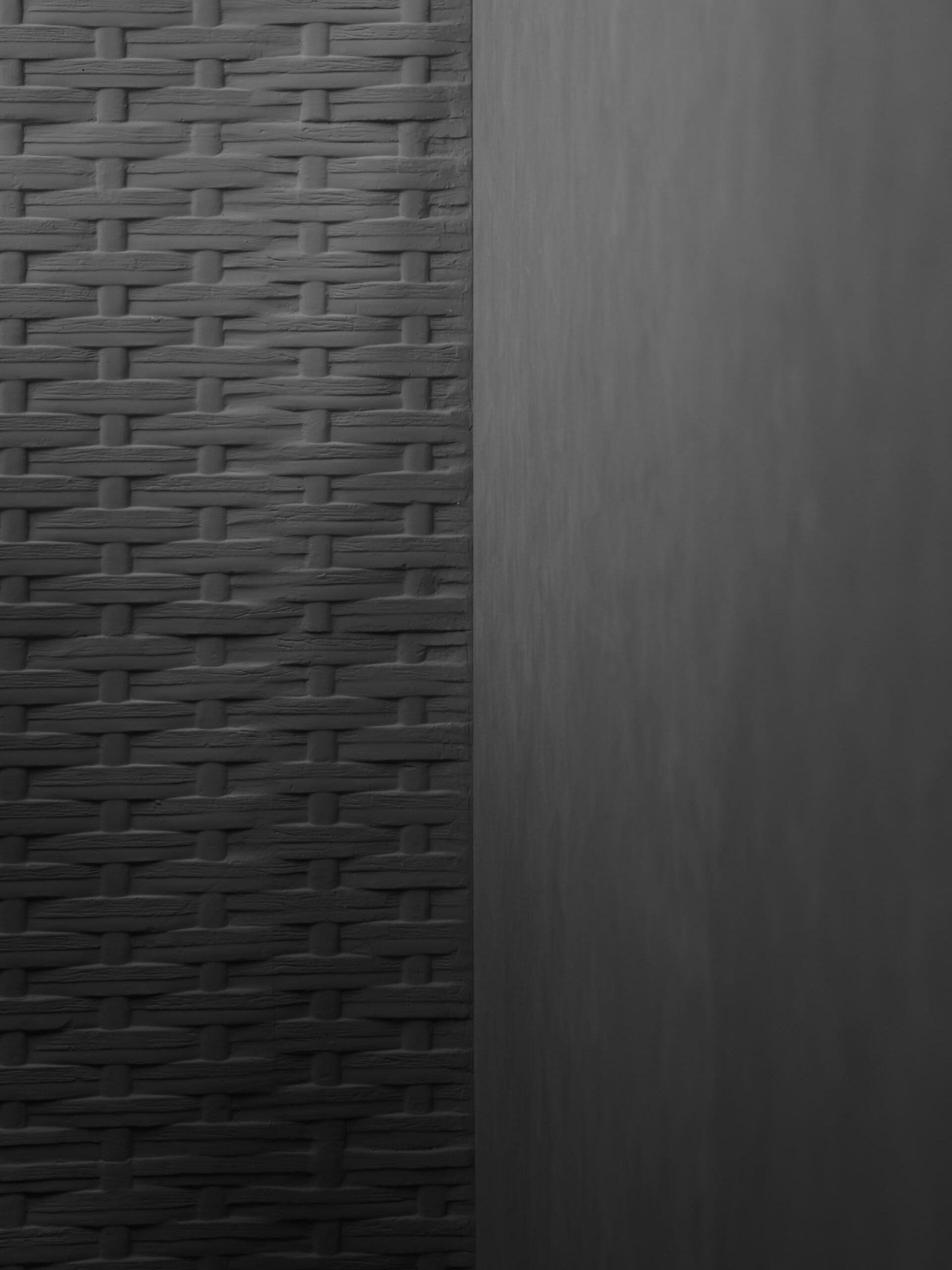 Black and white photo of junction detail between bamboo pressed concrete wall against plastered wall