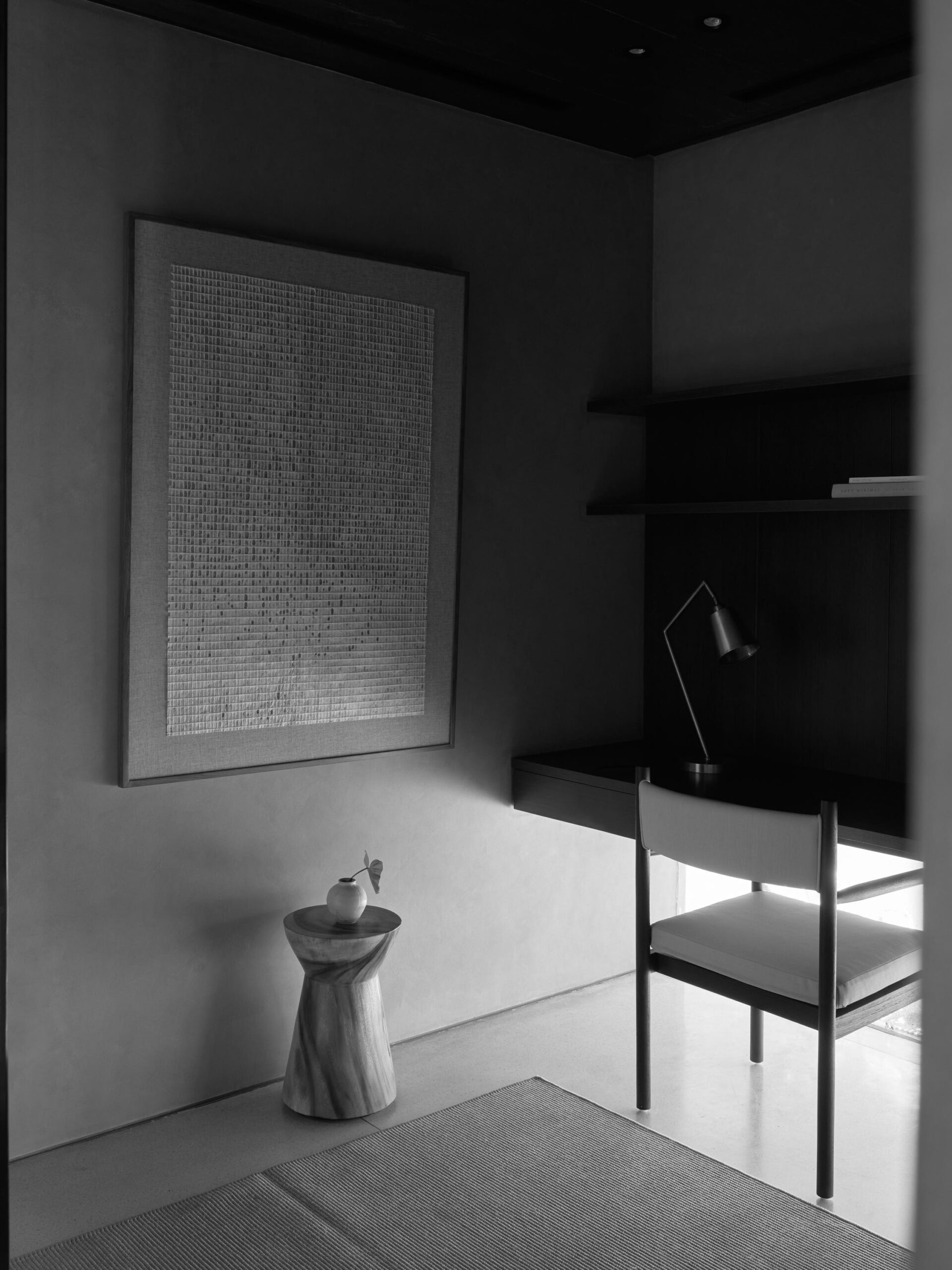 Black and white photo of a corner in the home office, showing working chair and banana paper artwork hanging on the wall